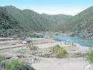 Green rafts on the sandy shore of a campsite, with cactus visible on the hillside across the river