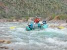 A man in orange life jacket and red top on a turquoise raft running through a rapid straight at the camera