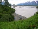 Looking down and across a river trip campsite with the broad river and snow covered mountains in the background
