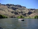 A gray raft on a smooth section of the Deschutes River with basalt cliffs in the background