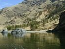 Looking across glassy green-gold water of the Snake River at an inviting beach