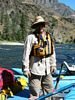 A man standing in a raft in long shirt and pants and straw hat