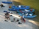 A rafting group camping on the beach in the evening light, with 3 rafts tied up beside them