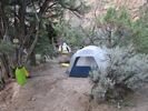 A dome tent tucked into a sheltered spot on obviously worn ground