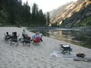 People sitting in folding chairs on a beach beside the Main Salmon River