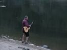 A guy peeing in the river with a guitarist over his shoulder